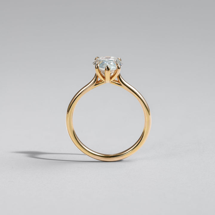A yellow gold solitaire engagement ring with a round brilliant-cut clear gemstone, shown from the back on a neutral gray background #material_gold