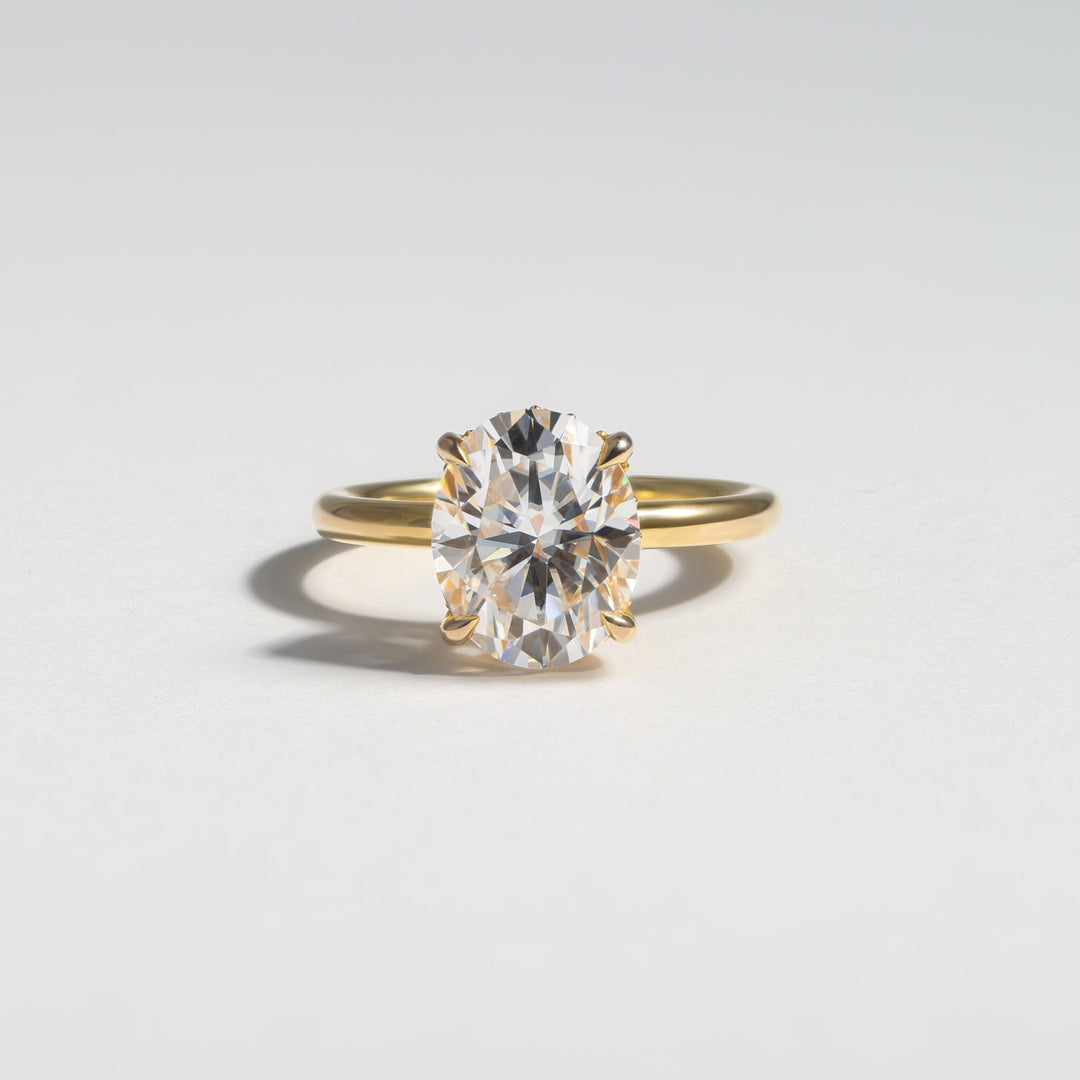 A yellow gold ring with a large oval-cut clear gemstone in a prong setting, photographed on a clean light gray background #material_gold
