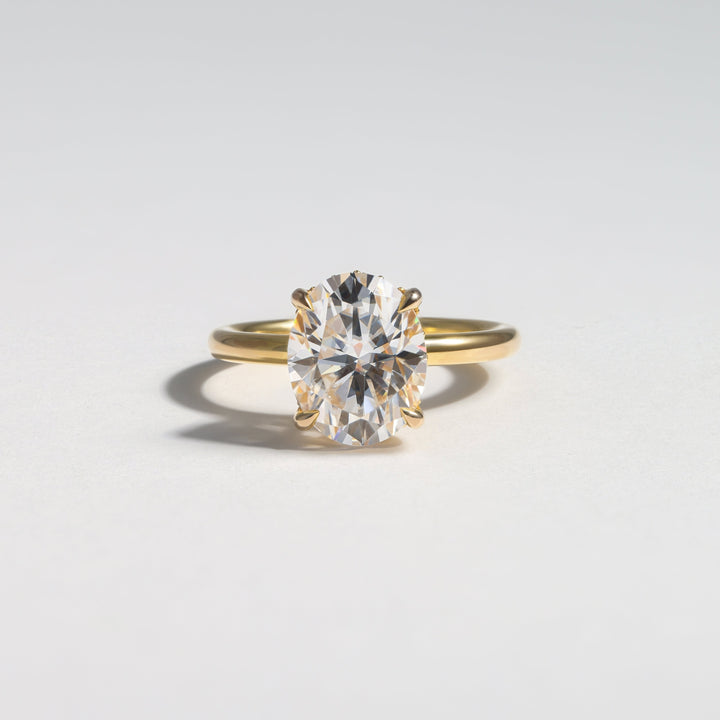 A yellow gold ring with a large oval-cut clear gemstone in a prong setting, photographed on a clean light gray background #material_gold
