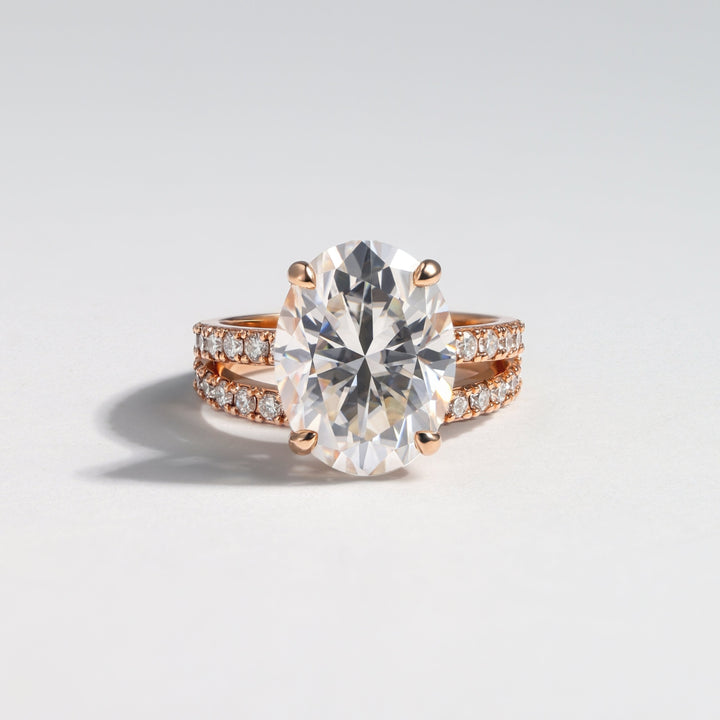 An oval-cut diamond engagement ring with a rose gold band accented by small pavé diamonds, photographed on a clean light gray background #material_rose