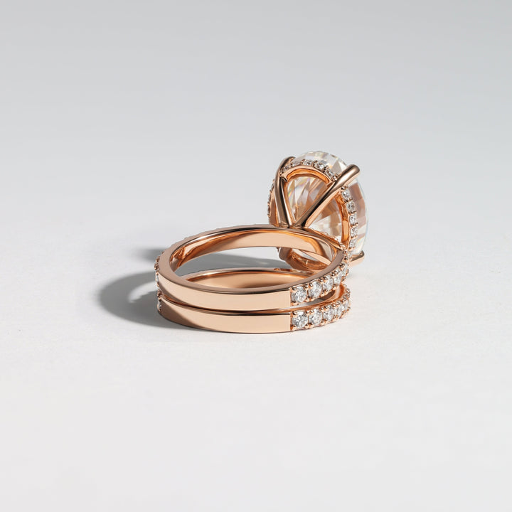 A rose gold ring set featuring a crown-shaped halo with a clear oval gemstone and a wrap-around band adorned with small clear stones, photographed on a light gray background #material_rose