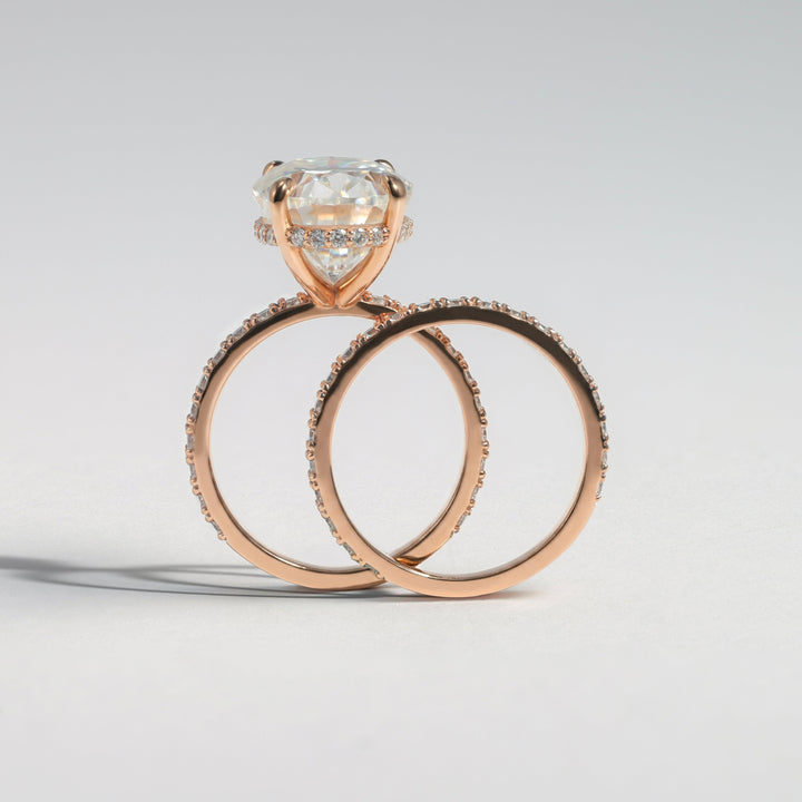 A rose gold engagement ring with a large round-cut clear gemstone and matching rose gold wedding bands with small pavé accents, photographed on a clean light gray background #material_rose
