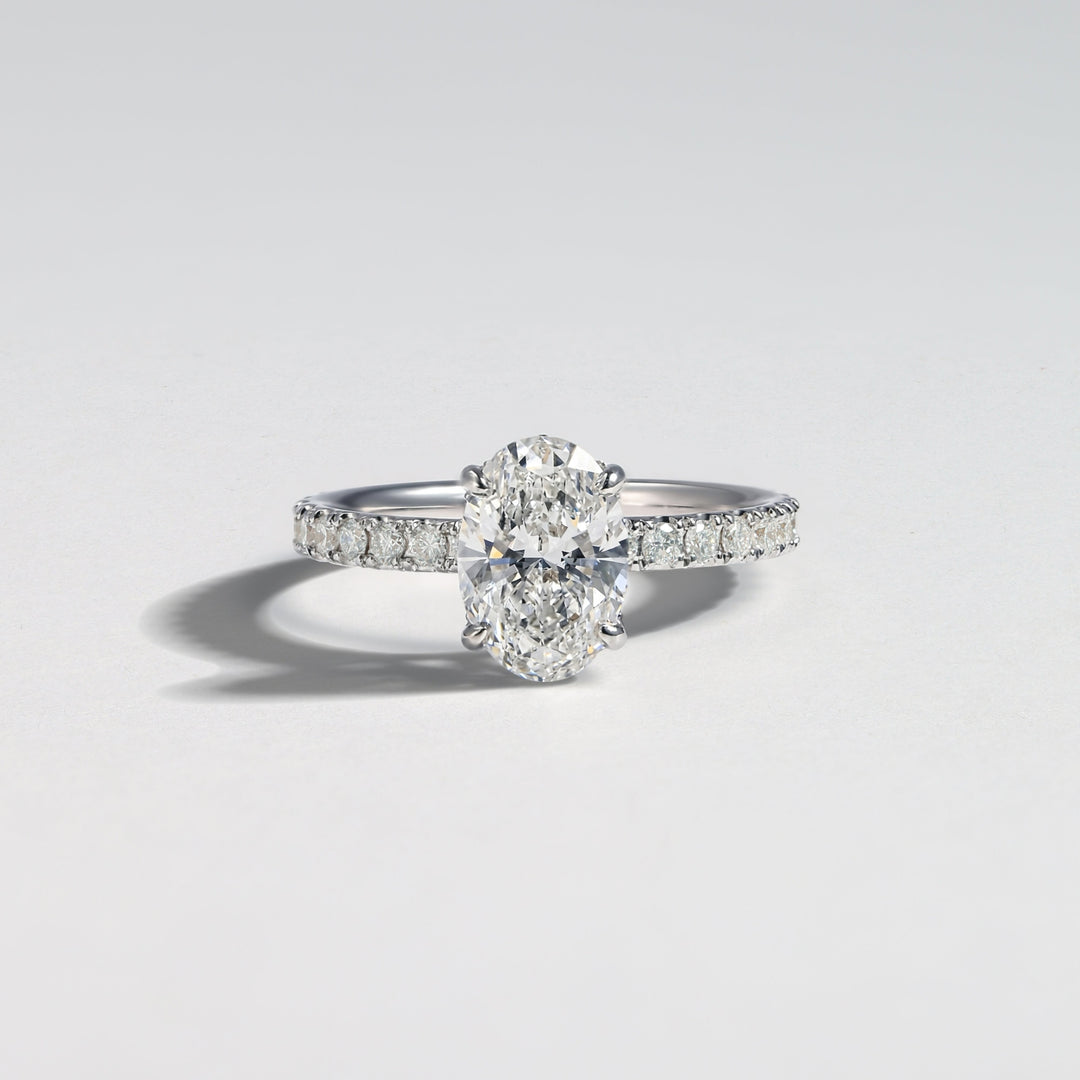 A diamond engagement ring with a round center stone and a pavé-set band, photographed on a clean light gray background #material_white