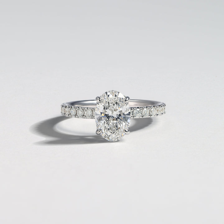 A diamond engagement ring with a round center stone and a pavé-set band, photographed on a clean light gray background #material_white
