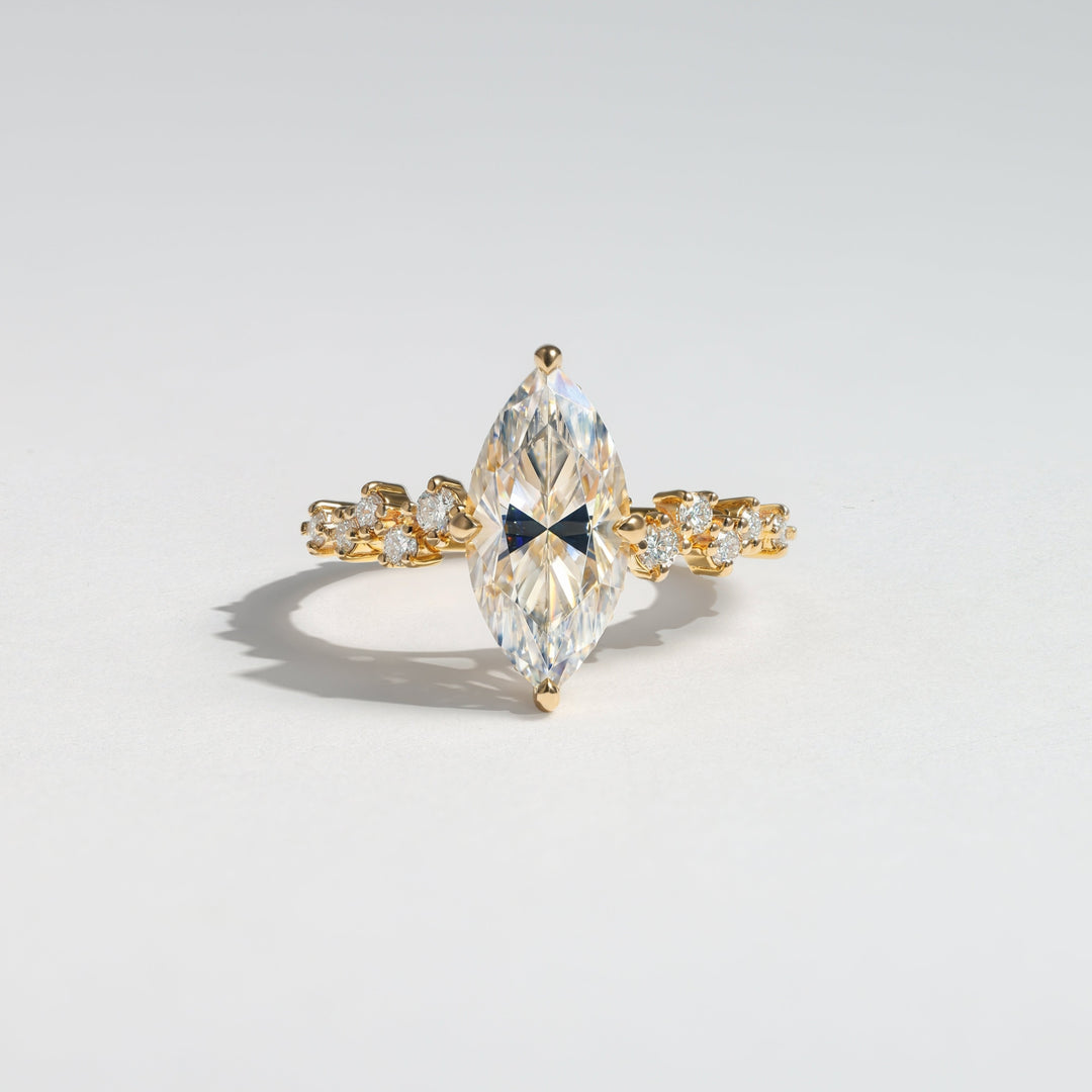 A gold ring featuring a large marquise-cut clear gemstone in the center, flanked by smaller clear stones along the band, photographed on a light gray background #material_gold