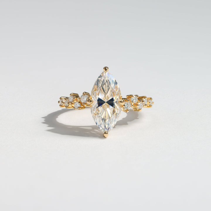 A gold ring featuring a large marquise-cut clear gemstone in the center, flanked by smaller clear stones along the band, photographed on a light gray background #material_gold