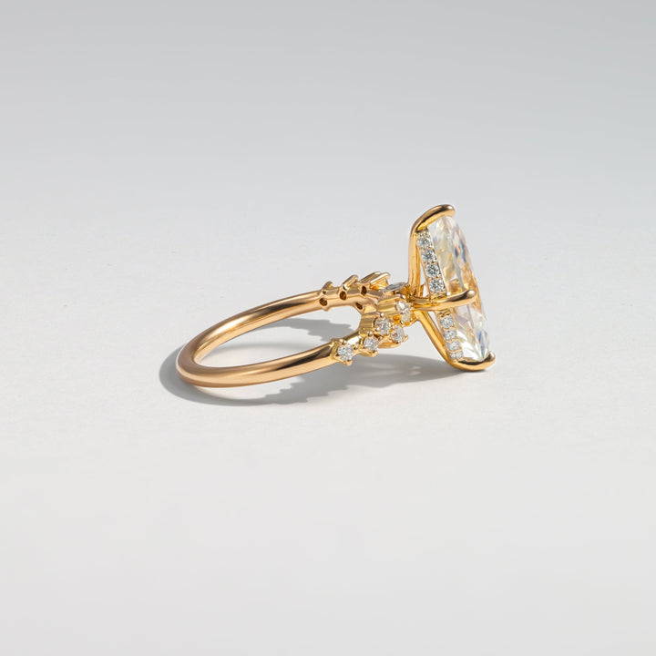 A gold ring with a large clear marquise-cut center stone and small clear accent stones on the band, photographed on a clean light gray background #material_gold