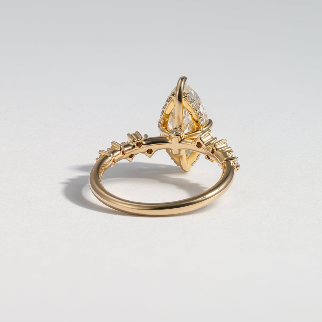 A gold ring with a unique marquise-cut gemstone held in a decorative setting, accented with small side stones, photographed on a light gray background #material_gold
