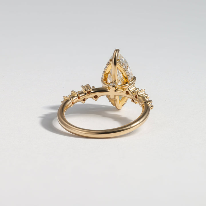 A gold ring with a unique marquise-cut gemstone held in a decorative setting, accented with small side stones, photographed on a light gray background #material_gold