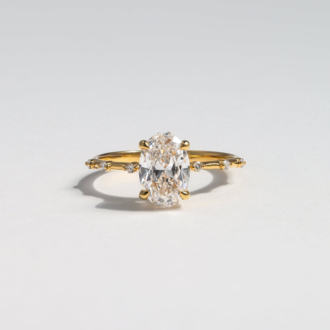 A yellow gold ring featuring a large oval-cut clear gemstone in a prong setting, with small side stones along the band, photographed on a light gray background #material_gold