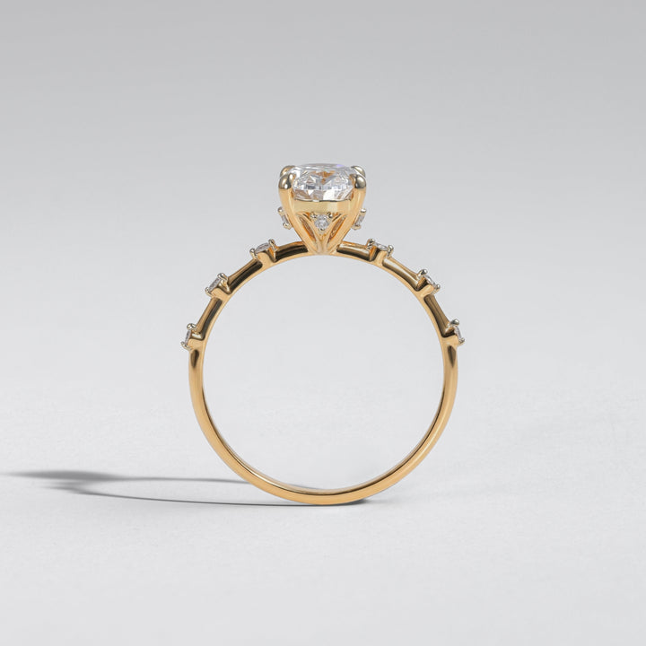 A yellow gold ring with a cushion-cut diamond center stone and small accent diamonds along the band, photographed on a neutral light gray background #material_gold