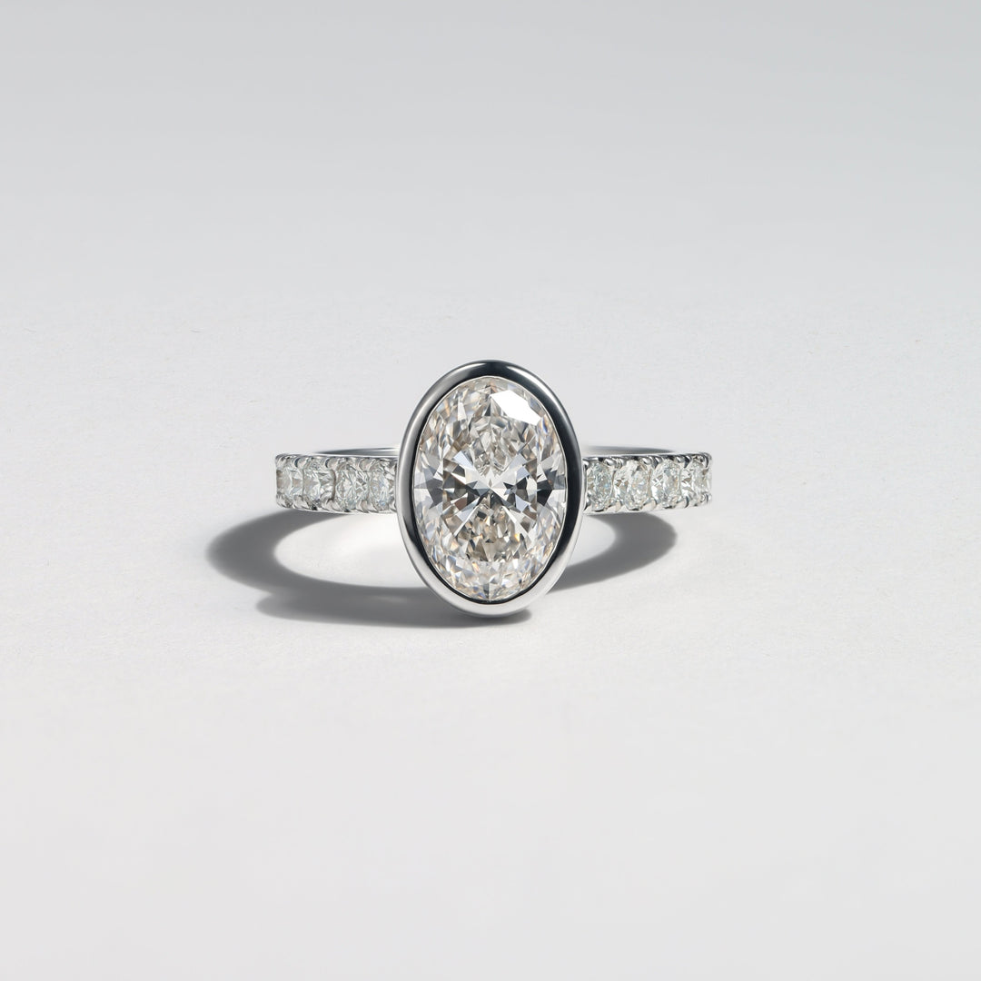 An oval diamond engagement ring with a silver-toned band featuring pavé-set diamonds, photographed on a clean light gray background #material_white