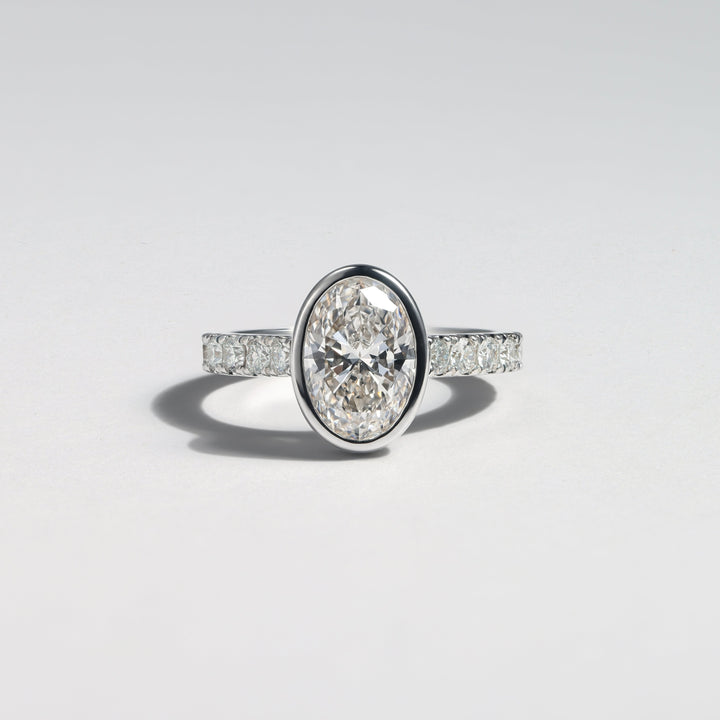 An oval diamond engagement ring with a silver-toned band featuring pavé-set diamonds, photographed on a clean light gray background #material_white