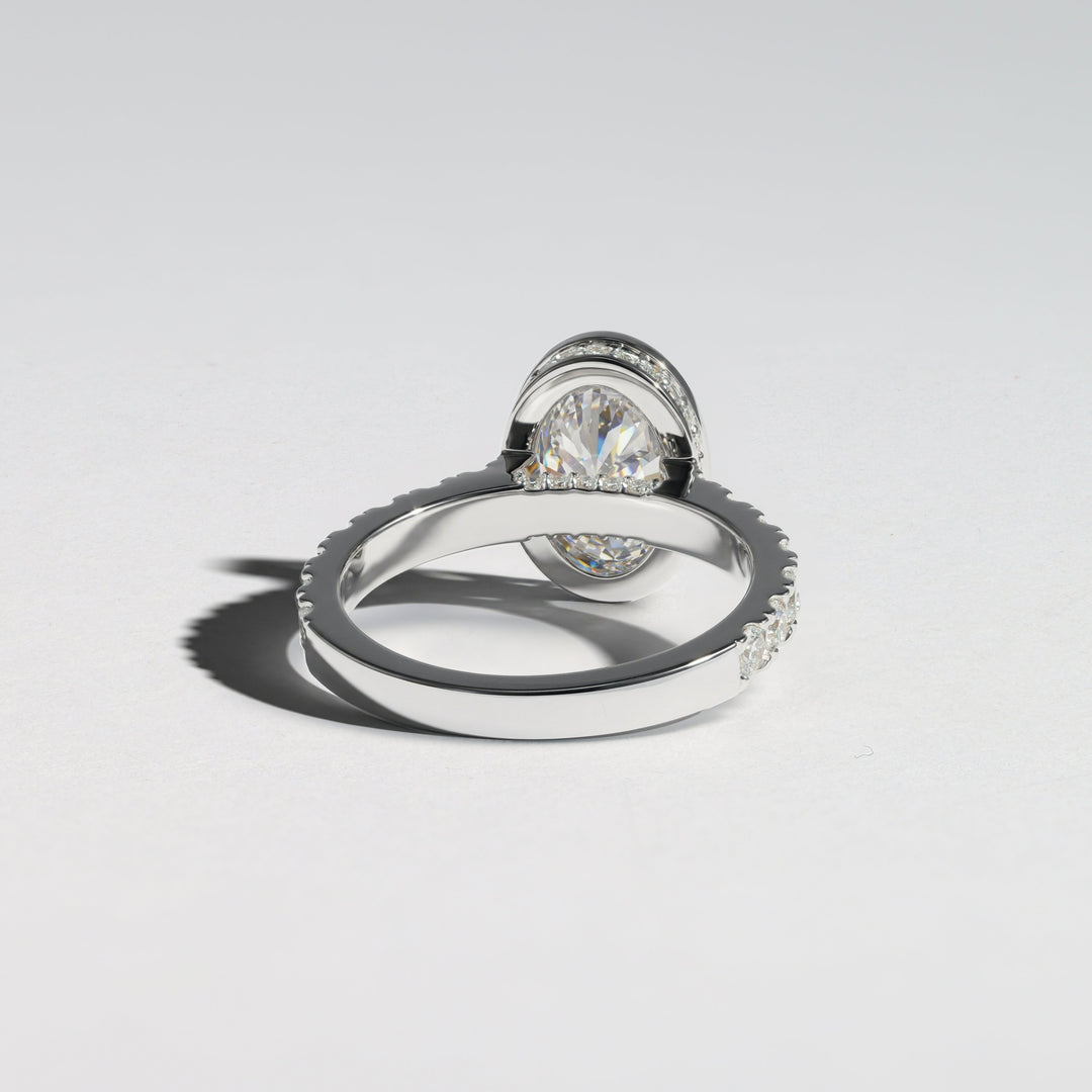 A silver-toned ring with a round clear gemstone in a halo setting, shown on a clean light gray background with a soft shadow #material_white