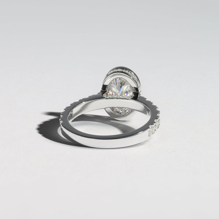 A silver-toned ring with a round clear gemstone in a halo setting, shown on a clean light gray background with a soft shadow #material_white