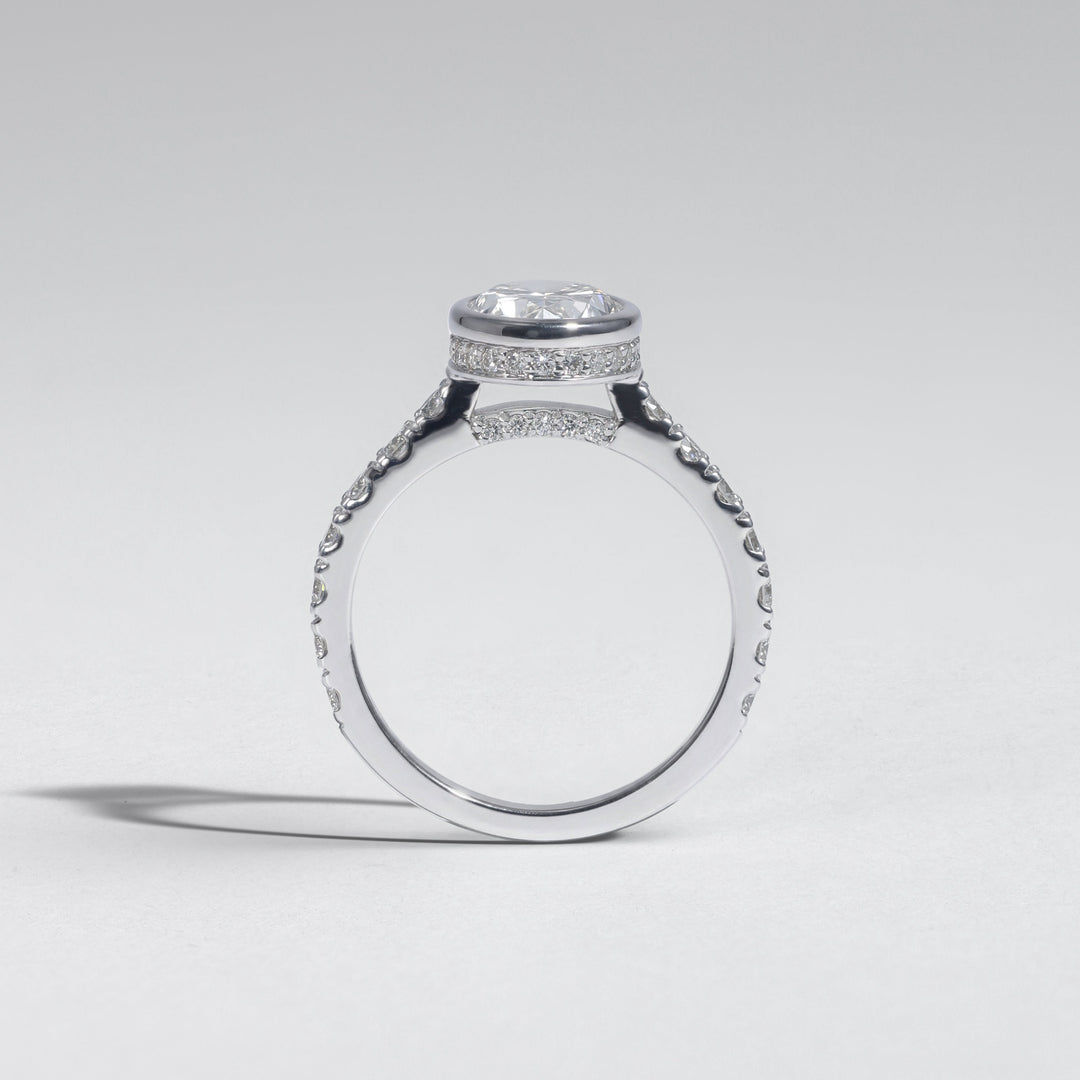 A silver-toned diamond ring with a oval-cut center stone and pavé-set side stones, shown from a side profile on a light gray background #material_white
