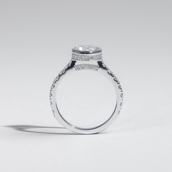 A silver-toned diamond ring with a oval-cut center stone and pavé-set side stones, shown from a side profile on a light gray background #material_white