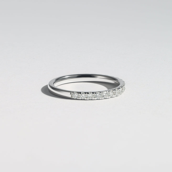 A slim silver band ring featuring a pavé-set row of clear stones on one side, photographed on a clean light gray background #material_white