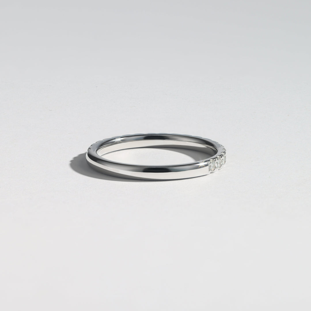 A minimalist silver band ring with a small row of clear stones on one end, photographed on a clean light gray background #material_white