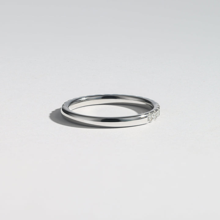 A minimalist silver band ring with a small row of clear stones on one end, photographed on a clean light gray background #material_white