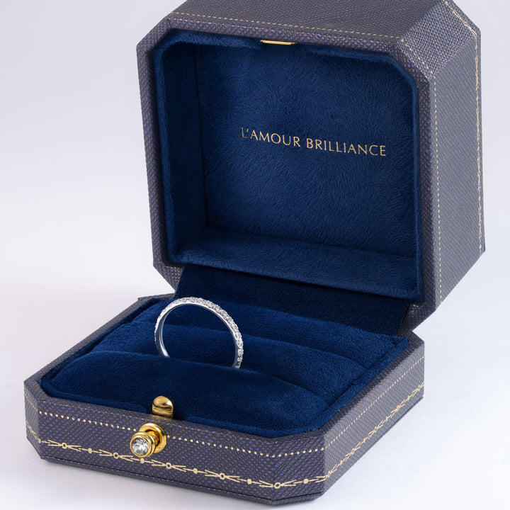 A silver band ring displayed inside an open textured navy blue jewelry box with a deep blue velvet interior. The inside lid features the gold-embossed brand name 'L'AMOUR BRILLIANCE'. #material_white