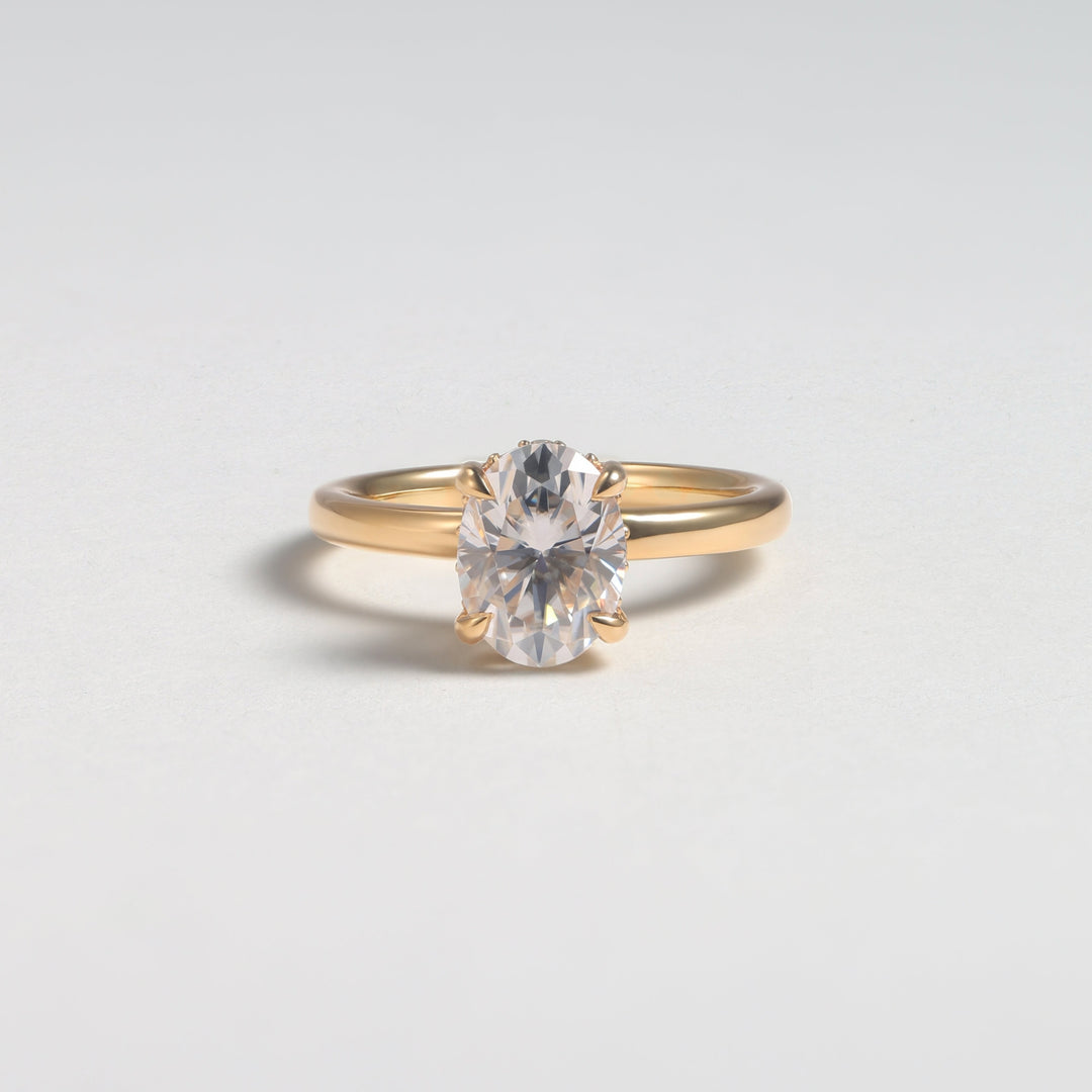 A gold solitaire engagement ring with a round brilliant-cut clear gemstone, photographed on a clean light gray background #material_gold