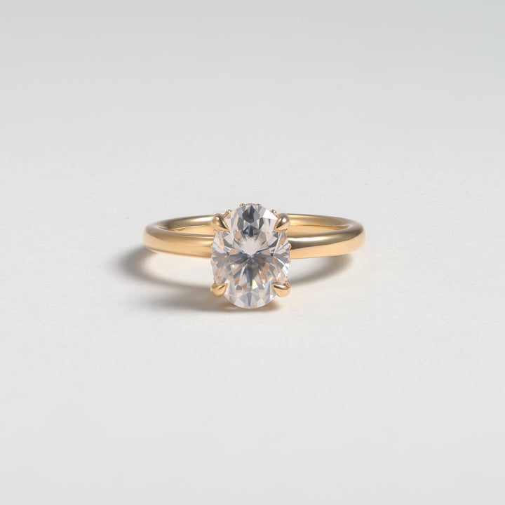 A gold solitaire engagement ring with a round brilliant-cut clear gemstone, photographed on a clean light gray background #material_gold