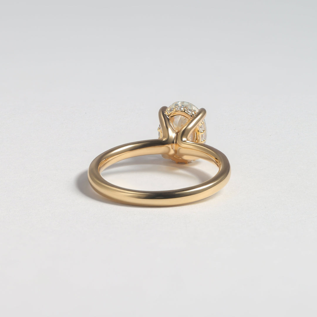 A gold ring with a diamond solitaire setting, photographed from a side angle on a clean, light gray background #material_gold