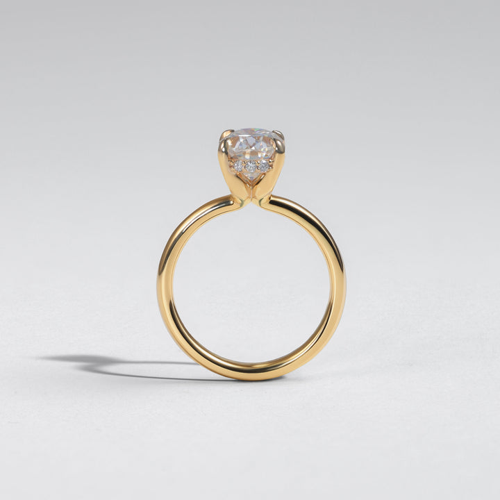 A yellow gold solitaire ring with a heart-shaped clear gemstone, photographed on a neutral light gray background #material_gold
