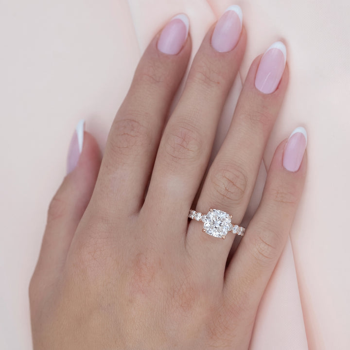 A close-up of a hand with pale pink and white French manicure, wearing a silver ring with a large cushion-cut diamond and smaller side diamonds, set against a soft pink background. #material_rose