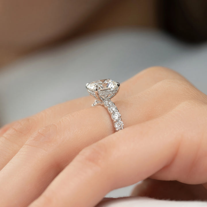 A close-up of a silver-toned engagement ring with a large heart-shaped clear gemstone and a pavé-set band, worn on a person's finger.#material_white