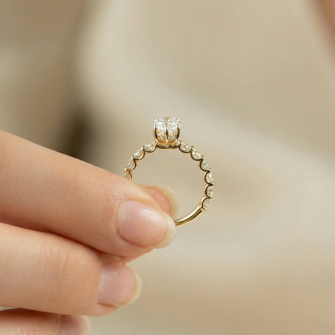 Gold ring with diamonds held between fingers against a blurred background #material_gold