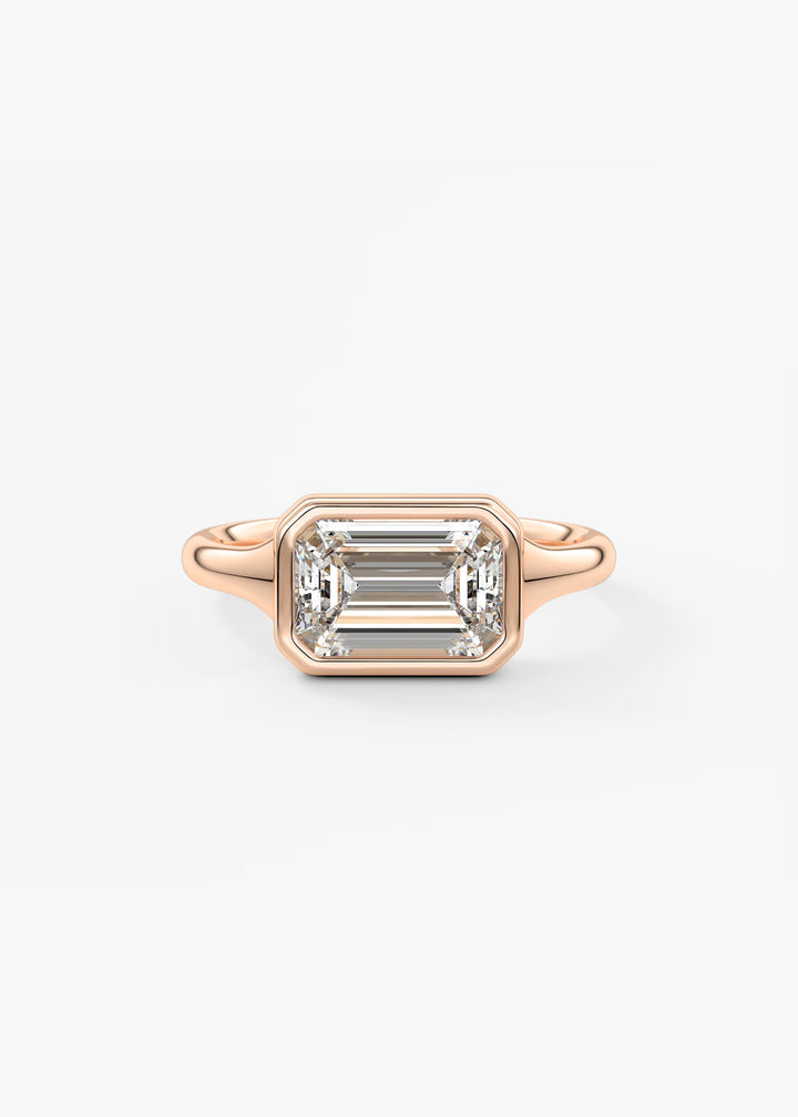 A rose gold ring featuring an emerald-cut clear gemstone in a bezel setting, shown against a plain white background.#material_rose