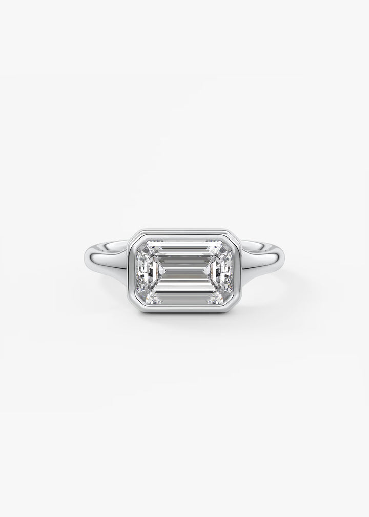 An emerald-cut diamond ring in a silver-toned metal setting, centered on a clean white background. #material_white