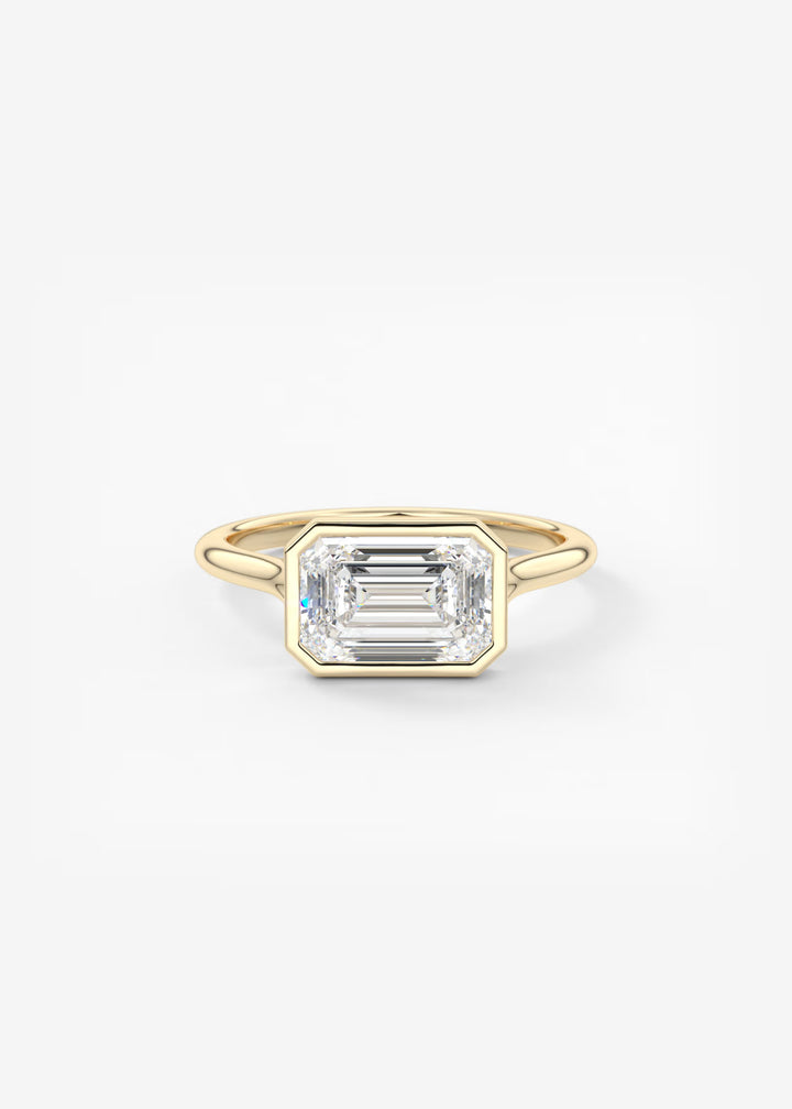 A yellow gold ring featuring a large, bezel-set emerald-cut clear gemstone, photographed against a seamless white background.#material_gold