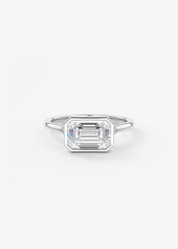 An emerald-cut diamond ring in a silver-toned metal band, centered on a clean white background. #material_white