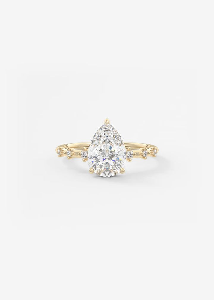 A pear-cut diamond engagement ring in yellow gold with small accent diamonds on the band, set against a clean white background.#material_gold