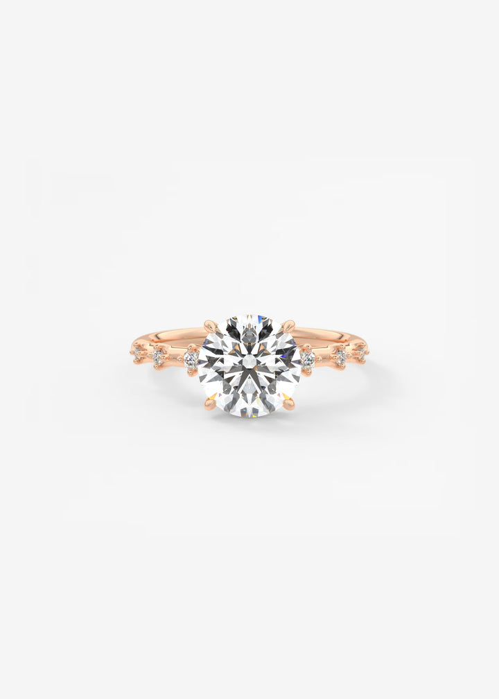 A rose gold engagement ring featuring a large round-cut clear center stone and smaller side stones, photographed on a clean white background.#material_rose
