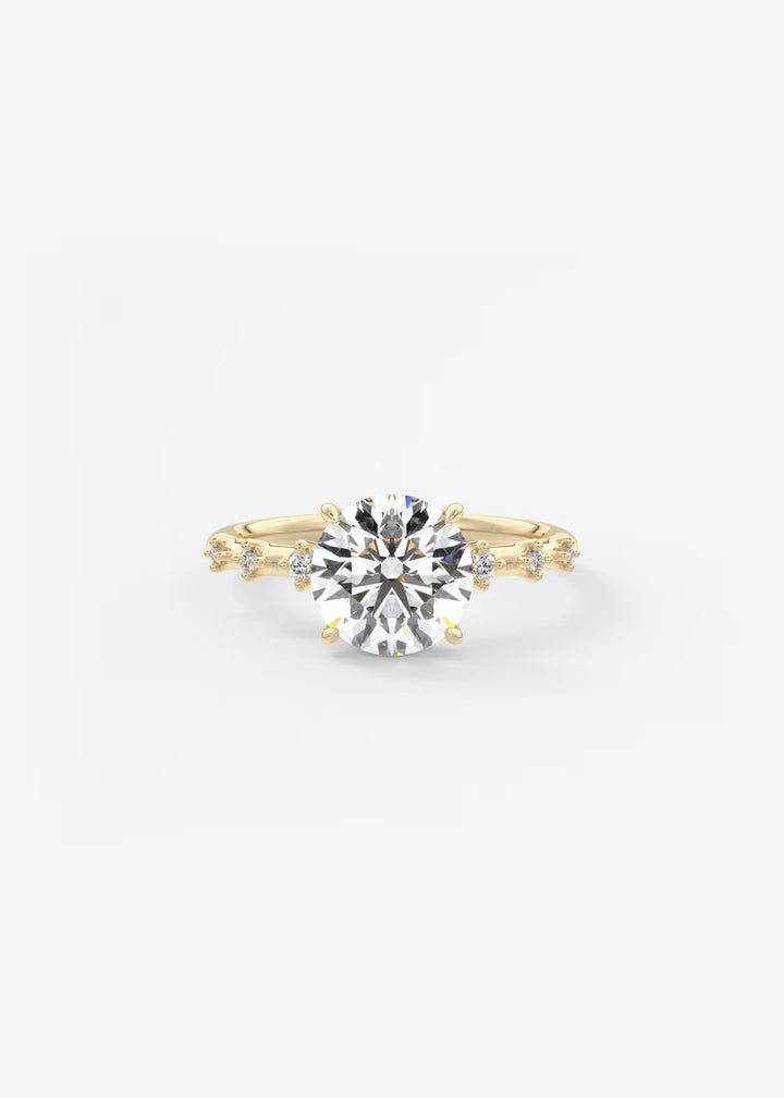 A yellow gold solitaire engagement ring with a round brilliant-cut center stone and small accent stones along the shoulders, set against a plain white background.#material_gold