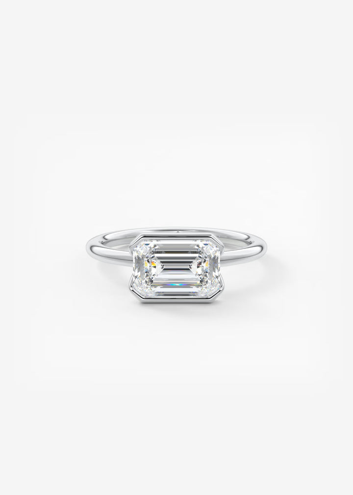 An emerald-cut diamond engagement ring in a silver-colored metal band, centered on a clean white background. #material_white