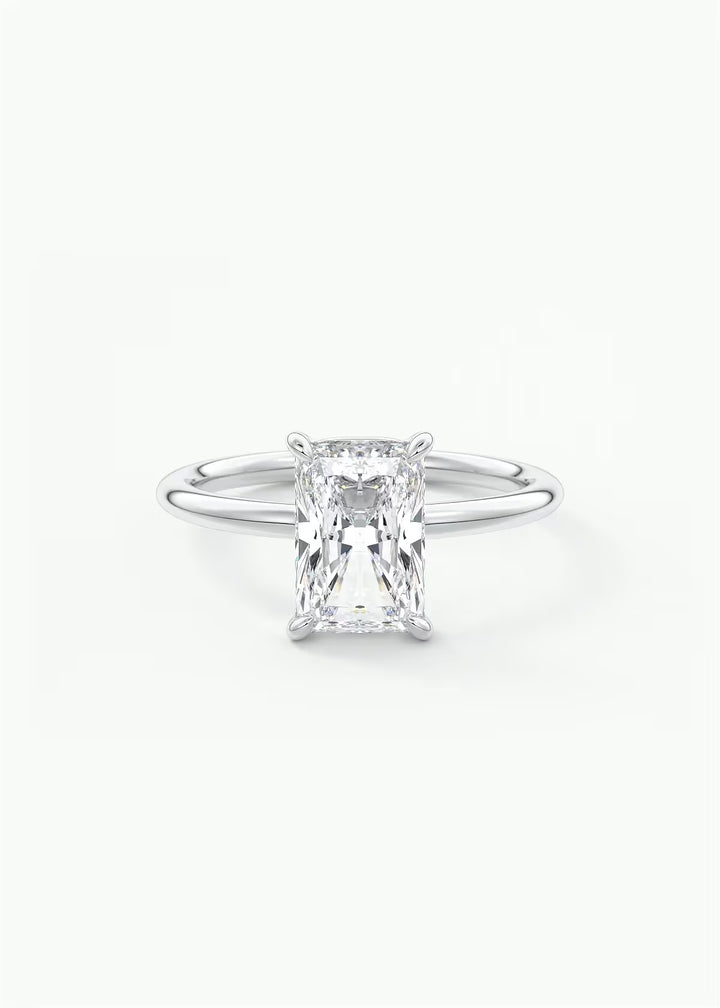 A silver solitaire engagement ring featuring a rectangular emerald-cut diamond, set against a clean white background. #material_white