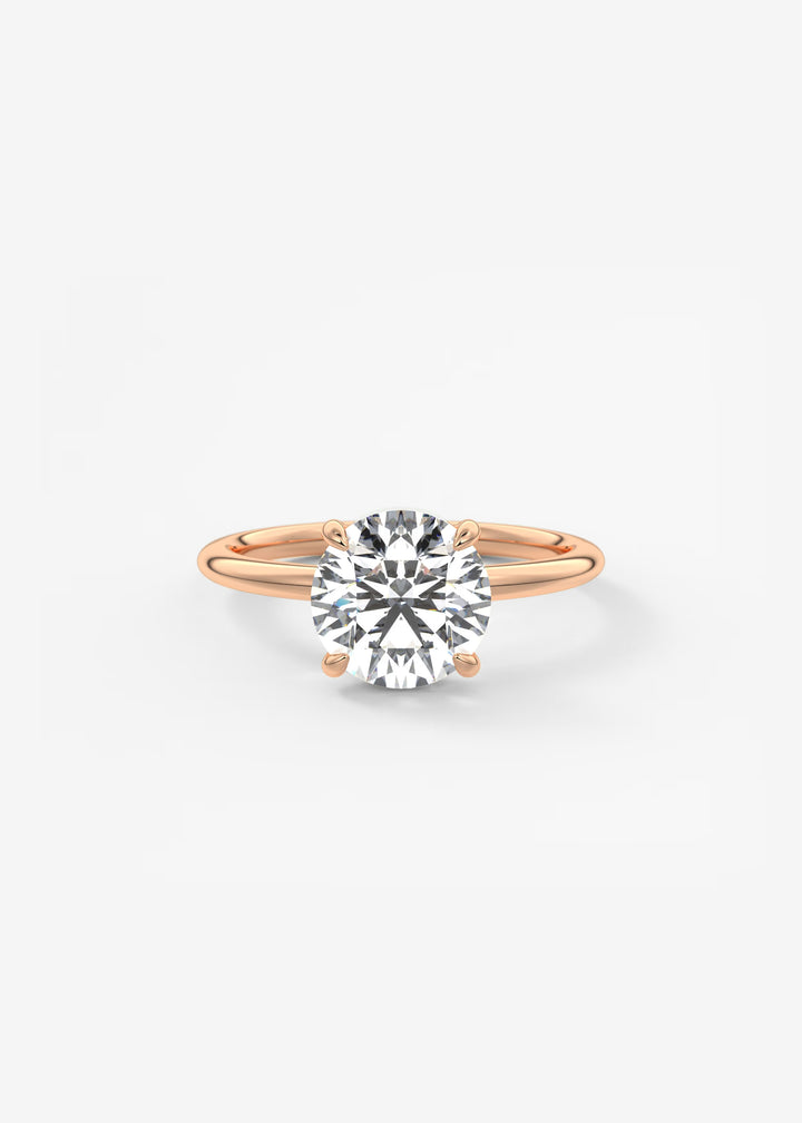 A classic solitaire engagement ring featuring a round brilliant-cut diamond set in a rose gold four-prong setting on a polished band, centered against a clean white background.#material_rose