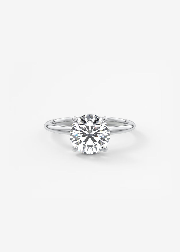 A classic solitaire engagement ring featuring a round brilliant-cut diamond set in a polished silver-colored metal band, centered on a clean white background.#material_white