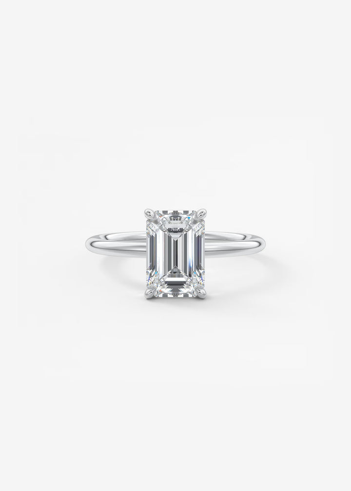 An emerald-cut diamond solitaire ring in a silver-colored metal setting, centered on a clean white background.#material_white