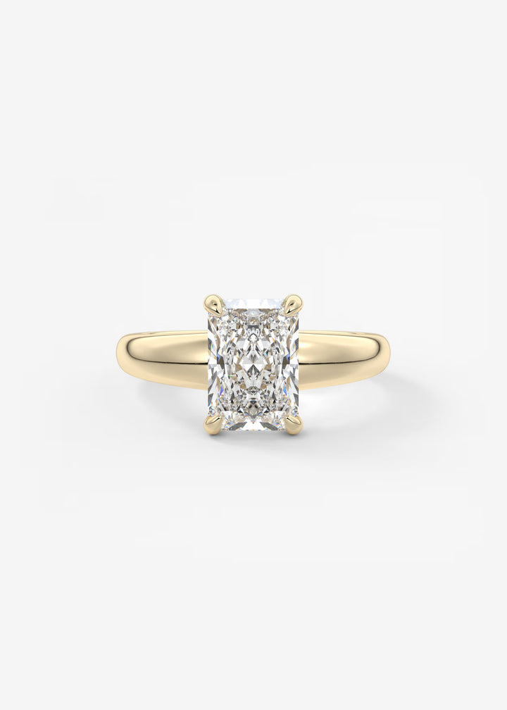 A yellow gold solitaire ring featuring a large rectangular radiant-cut diamond, set against a clean white background.#material_gold