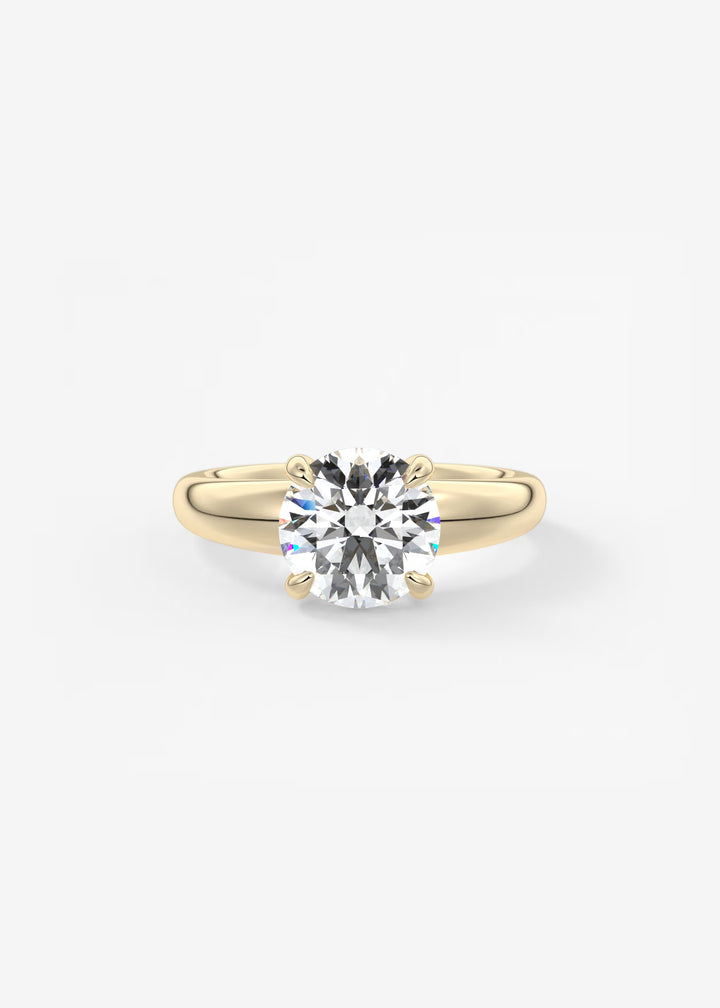A classic solitaire engagement ring featuring a round brilliant-cut diamond set in a yellow gold four-prong band, centered on a clean white background.#material_gold