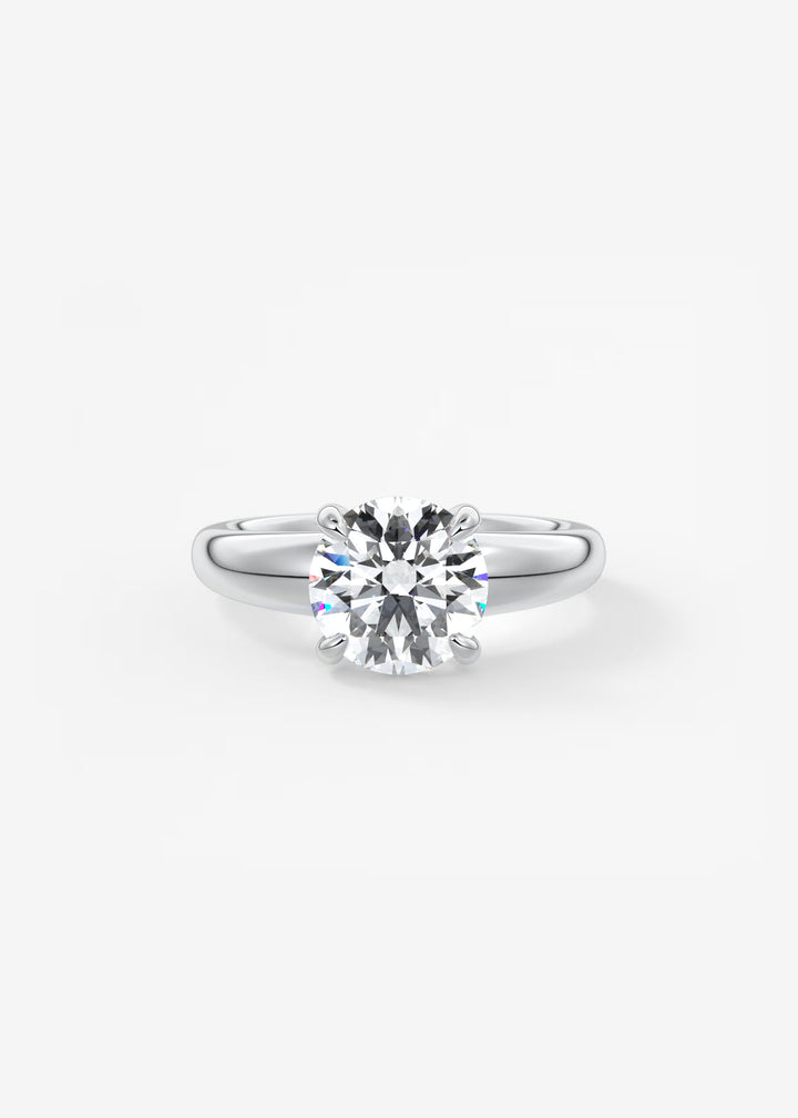 A classic solitaire engagement ring featuring a round brilliant-cut diamond set in a polished silver-colored band, presented on a clean white background.#material_white