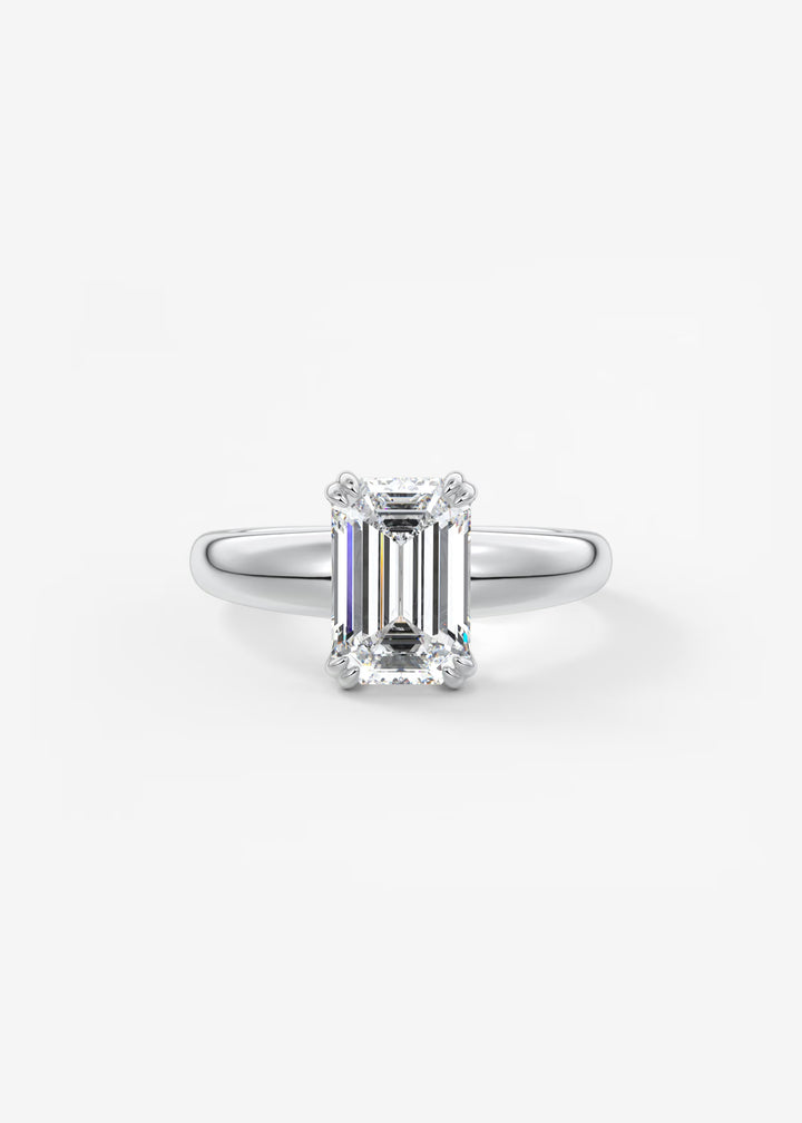 An emerald-cut diamond ring in a silver four-prong setting, centered on a clean white background.#material_white