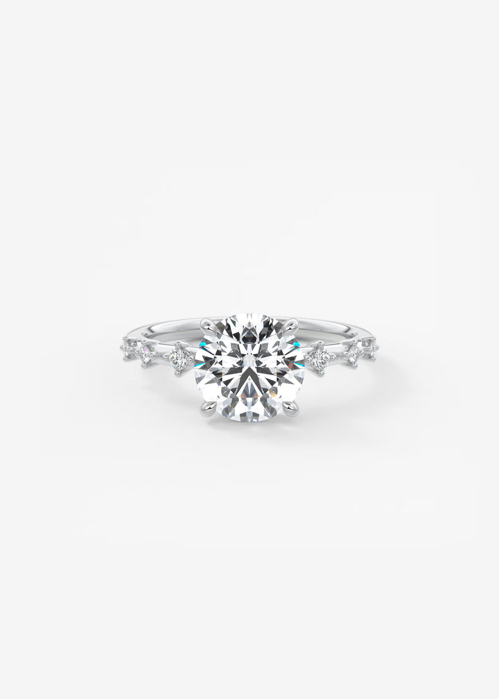A silver-toned diamond engagement ring featuring a large round-cut center stone and smaller diamonds along the band, set against a clean white background.#material_white