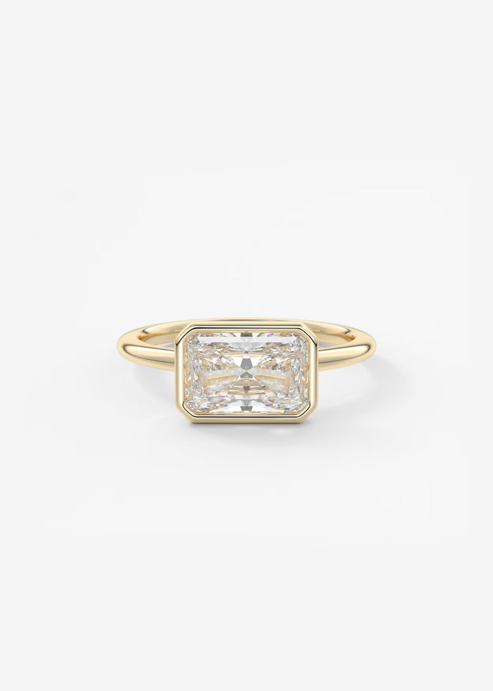 A yellow gold ring featuring a large rectangular emerald-cut diamond center stone, set against a clean white background.#material_gold